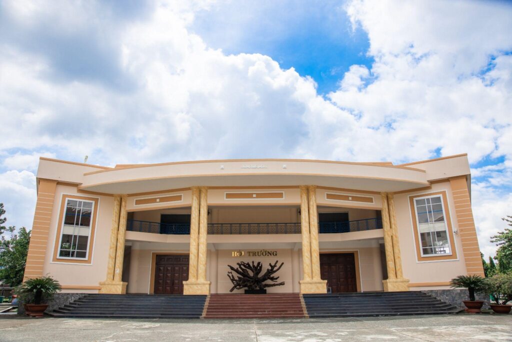 Đại học ngân hàng, tòa nhà lớn màu trắng với kiến trúc cổ điển, có cột trụ và mái cong, nằm trên một ngọn đồi. Trước tòa nhà có một sân rộng và một cây cổ thụ lớn.