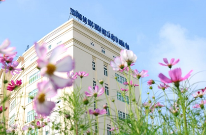 Tòa nhà Trường Đại học Khoa học Xã hội và Nhân văn TP.HCM, với màu trắng chủ đạo và hoa nở rộ trước mặt.