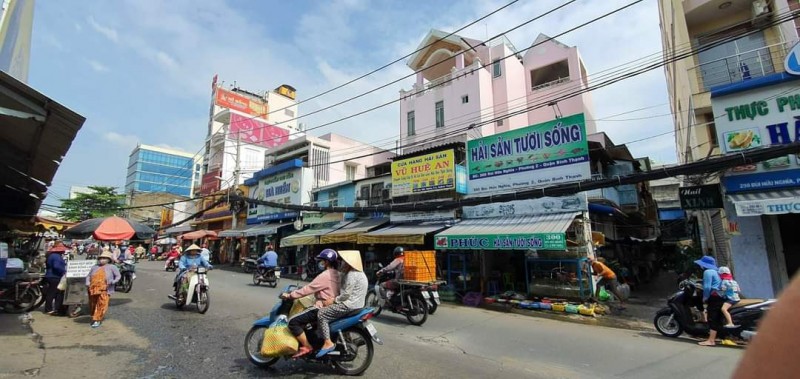 Chợ và khu phố kinh doanh trên đường Bùi Hữu Nghĩa, quận Bình Thạnh, TP.HCM với xe máy và người dân tấp nập.