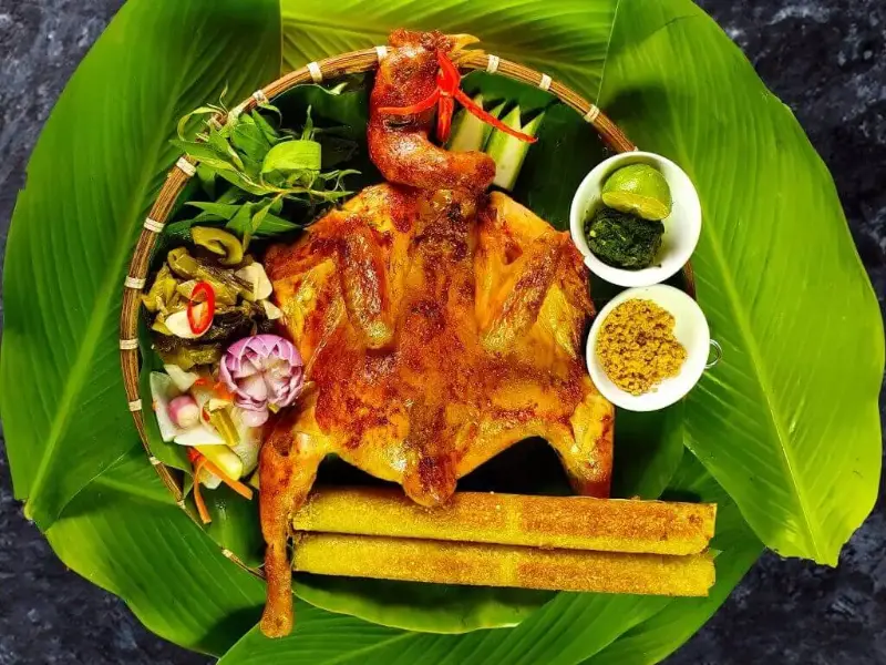 Món gà nướng cơm lam Đà Lạt được bày trí đẹp mắt trên mẹt lá chuối, gồm gà nướng vàng óng, cơm lam ống tre và các loại rau rừng ăn kèm.