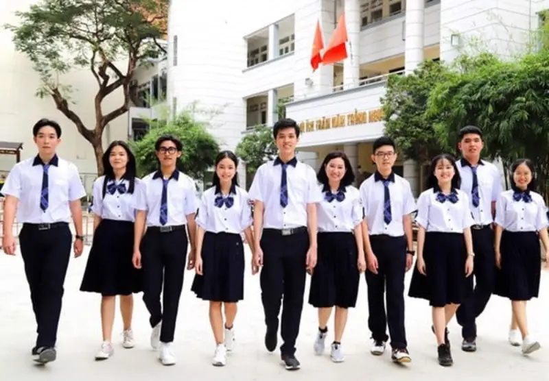 Nhóm học sinh Trường THPT Bùi Thị Xuân mặc đồng phục trắng xanh, bước đi tự tin trong khuôn viên trường với tòa nhà chính phía sau.