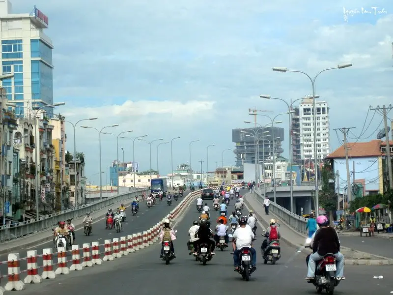 Nhiều phương tiện xe máy và ô tô di chuyển trên Cầu Calmette vào ban ngày, khung cảnh đô thị xung quanh nhộn nhịp.