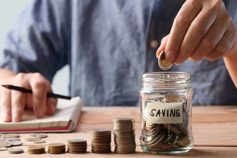 Người đang ghi chép và bỏ tiền xu vào hũ tiết kiệm, minh họa cho mẹo tiết kiệm chi phí thuê trọ hiệu quả