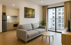 Phòng khách căn hộ chung cư hiện đại với sofa xám, bàn trà gỗ, tranh treo tường, cửa kính lớn mở ra ban công hướng nhìn sang các tòa nhà bên cạnh.