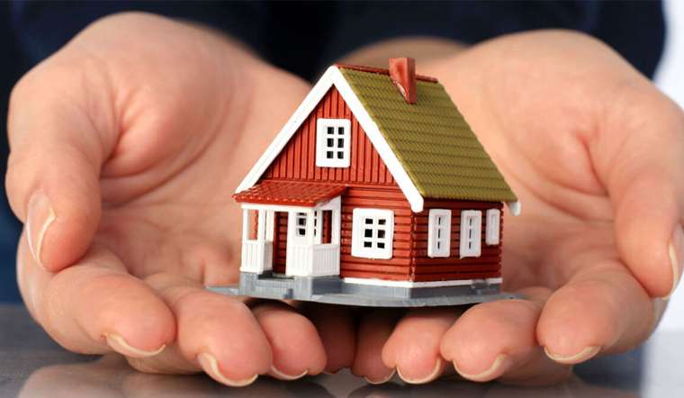 Một người đang nâng niu mô hình căn nhà nhỏ màu đỏ bằng cả hai tay.