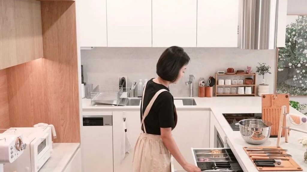 Người phụ nữ tóc ngắn đứng nhìn vào ngăn đựng dụng cụ ăn uống giữa phòng bếp gọn gàng