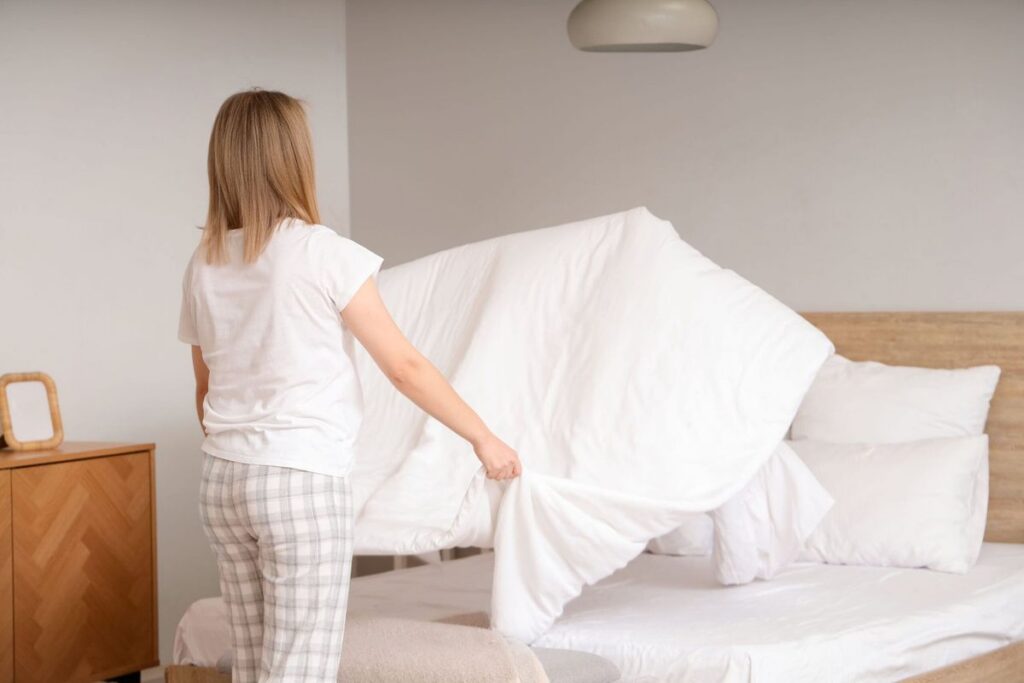Cô gái tóc vàng áo trắng quần caro đang gấp chăn màu trắng