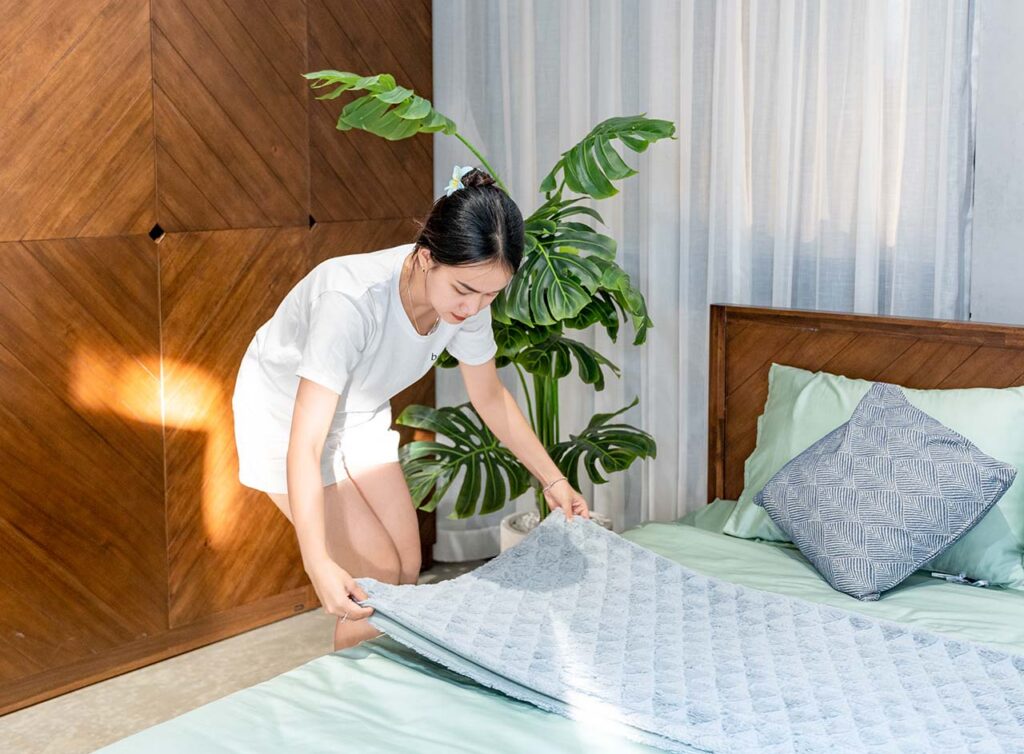 cô gái mặc đồ trắng đang gấp chăn màu xanh