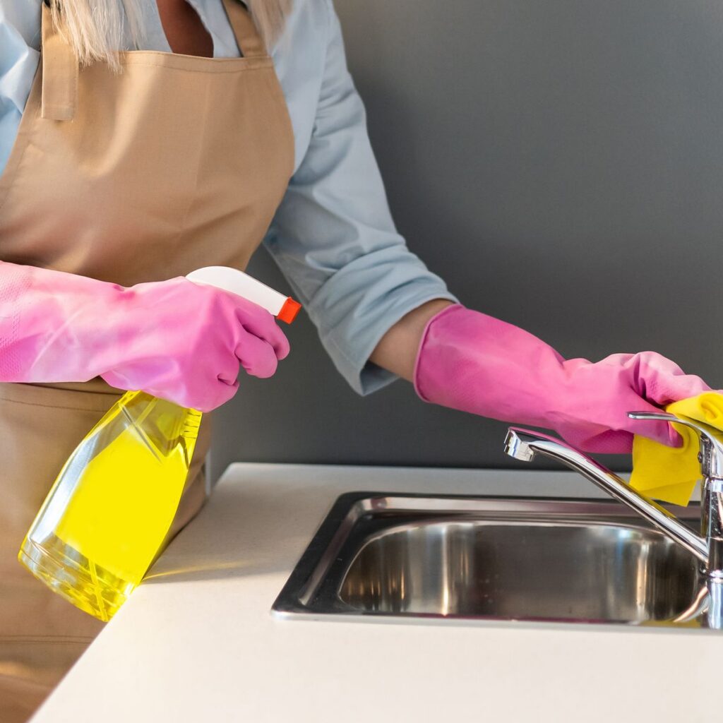 Người đeo găng tay hồng cầm bình xịt tẩy rửa để vệ sinh lavabo