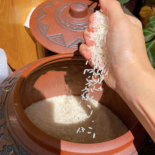 hũ gạo với gạo trắng đầy tay, biểu trưng cho sự đủ đầy, ổn định và ấm no trong gia đình.