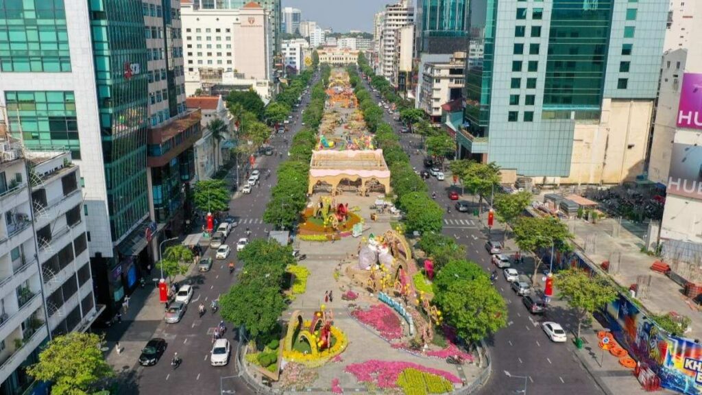 Góc nhìn từ trên cao xuống Phố đi bộ Nguyễn Huệ trải dài với những bồn hoa rực rỡ, các tòa nhà cao tầng hiện đại hai bên và dòng người tham quan tản bộ.