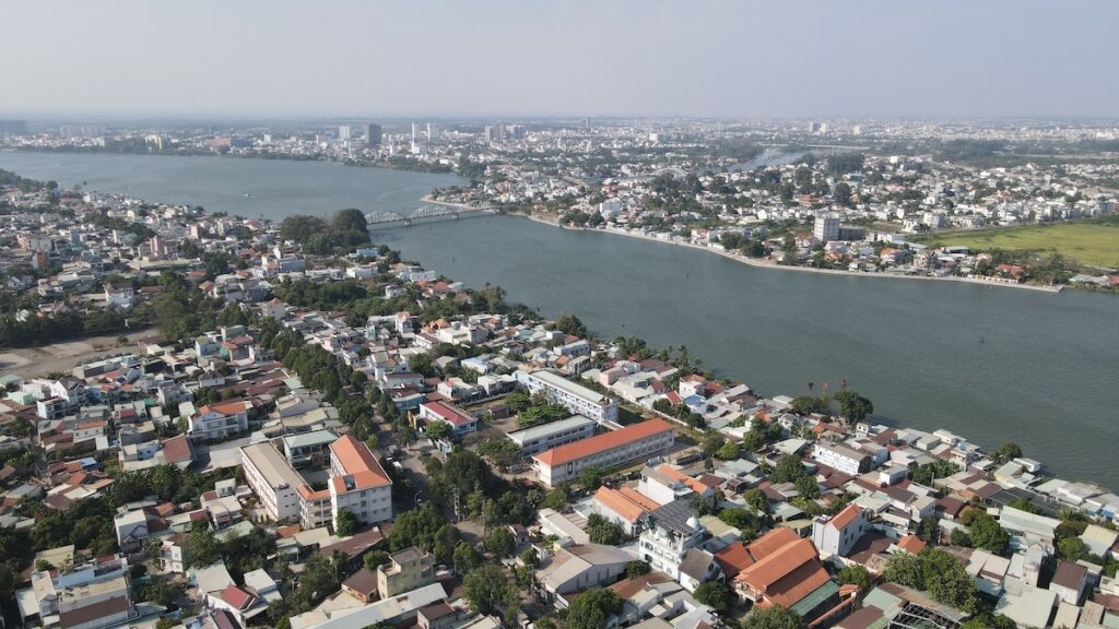 Khu dân cư ven sông với nhiều nhà thấp tầng và cầu bắc qua sông nhìn từ trên cao