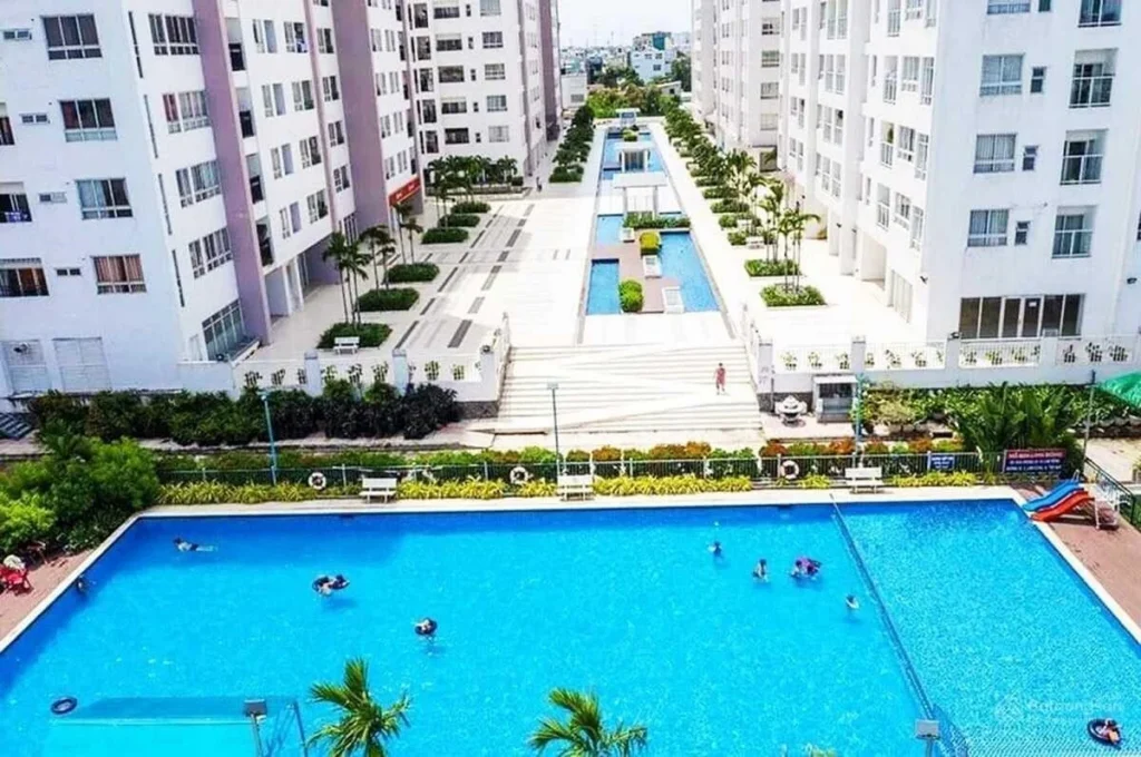 Khu vực hồ bơi lớn uốn lượn tại nội khu 4S Linh Đông, bên cạnh là lối đi bộ dải sỏi, cây nhiệt đới và các khu vực ghế nghỉ cho cư dân