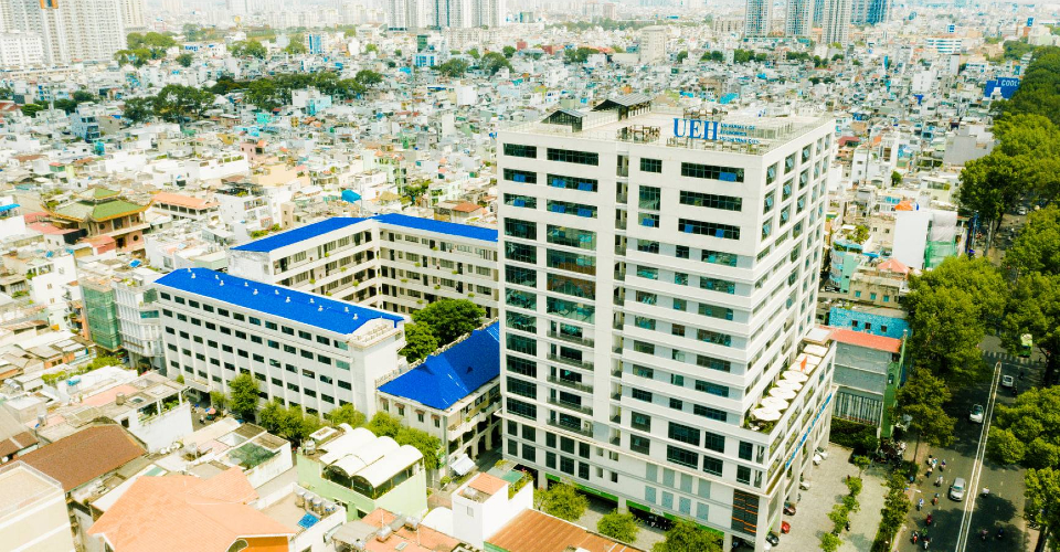 Khuôn viên Trường Đại học Kinh tế TP.HCM UEH với logo xanh lá và đài phun nước phía trước tòa nhà chính
