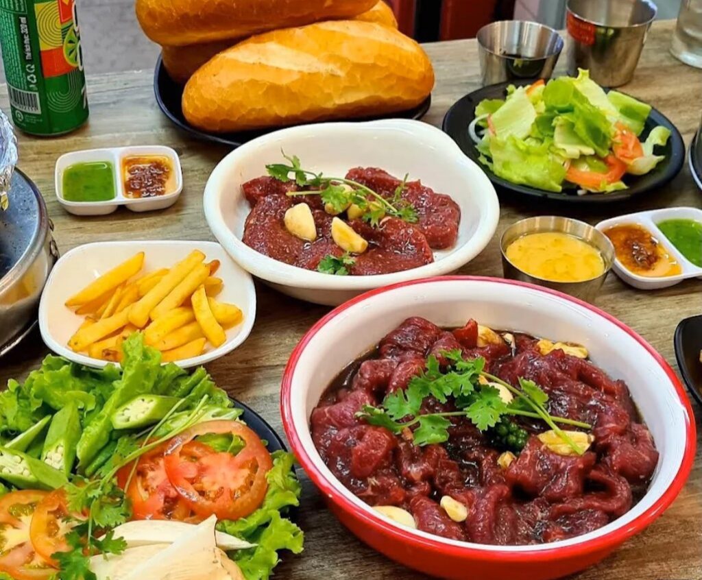 Đĩa thịt bò tươi xắt mỏng ướp gia vị băm nhỏ xếp đều đặn cạnh bếp nướng than hồng đặt tại bàn.