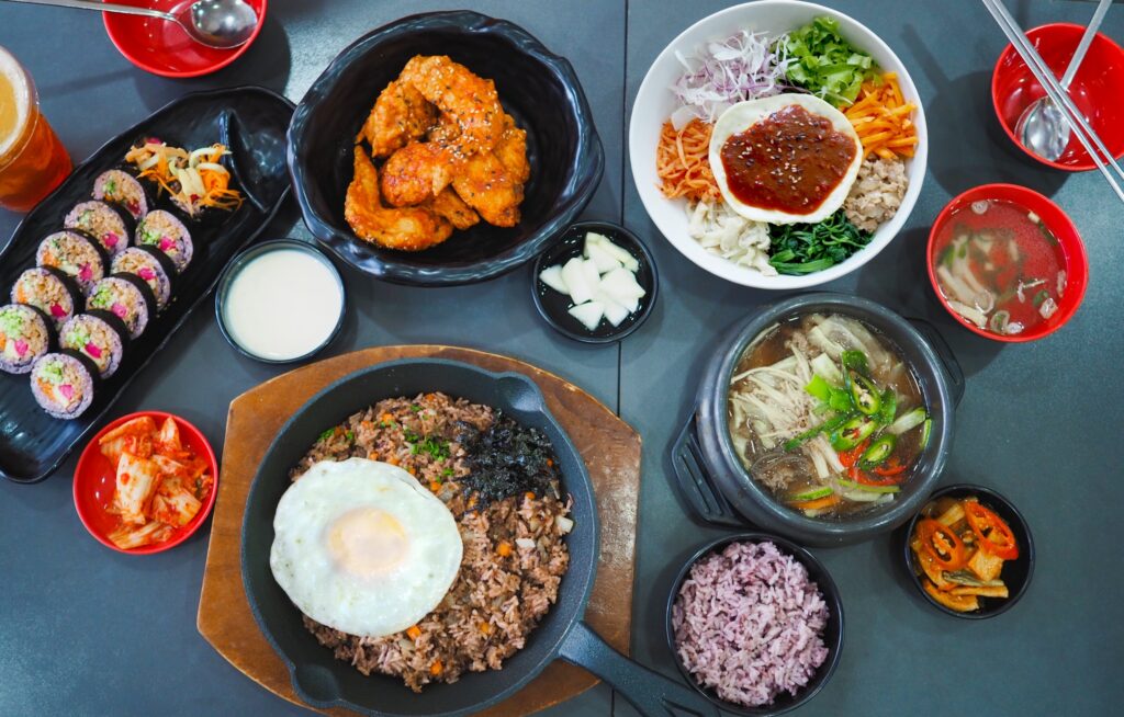 Mặt tiền nhà hàng Hanuri Korean Fast Food với biển hiệu màu vàng đen đặc trưng, các poster món ăn Hàn Quốc và hệ thống cửa kính.