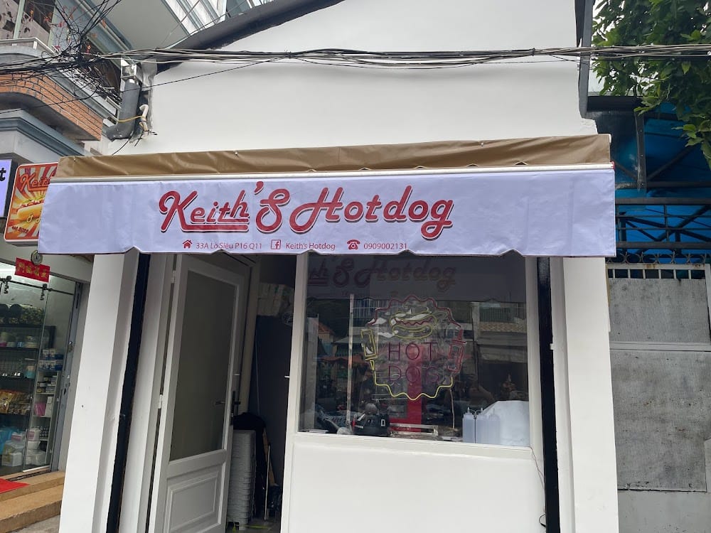 Quầy kệ và mặt tiền tiệm Keith's HotDog với biển hiệu tối giản, trưng bày menu các loại xúc xích và bánh mì.
