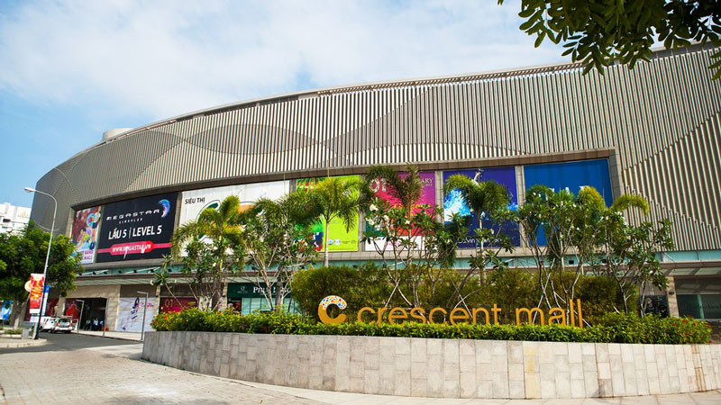 Mặt tiền vòm kính cong hiện đại nhiều tầng của trung tâm thương mại Crescent Mall hướng lối đi bộ rộng rãi bên hông hồ.