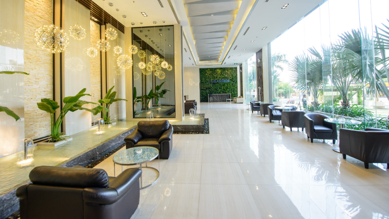 Không gian sảnh đón khách sang trọng rộng rãi tại chung cư An Gia Garden Tân Phú với trần cao, đèn chùm trang trí hiện đại, tiểu cảnh thác nước và hệ kính lớn đón sáng