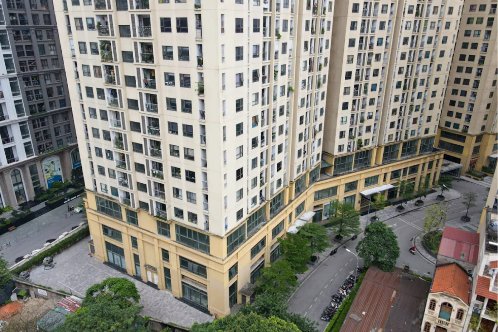 Góc chụp từ trên cao cận cảnh một block tòa nhà chung cư cao tầng thực tế với các ô cửa sổ và ban công san sát nhau, phía dưới chân tòa nhà là đường nội bộ