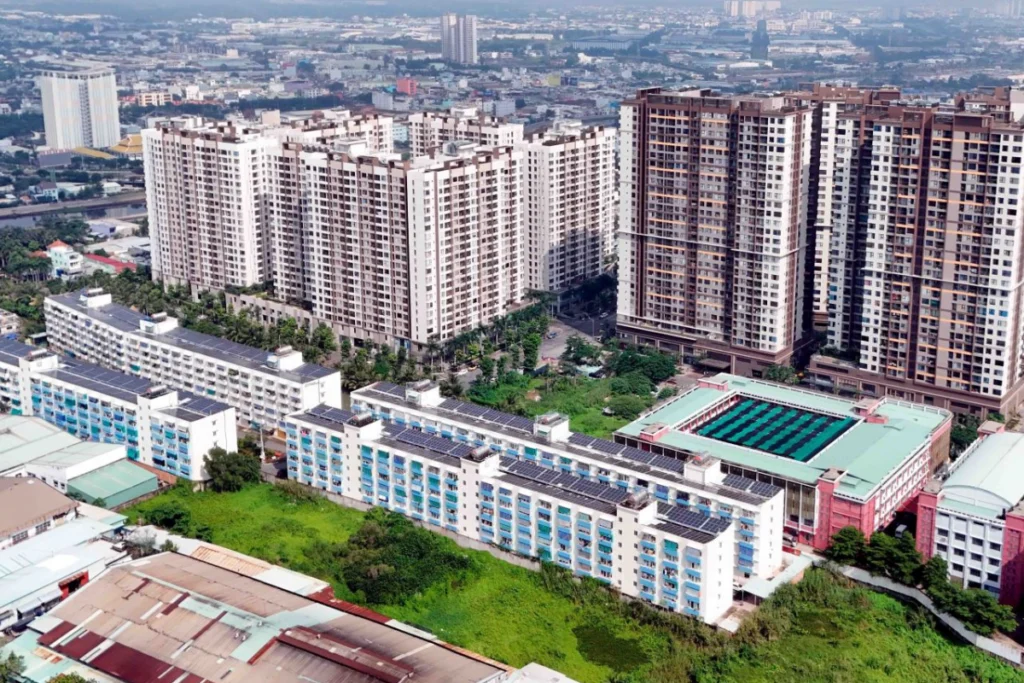 Góc nhìn từ trên cao xuống một tổ hợp khu đô thị hiện đại bao gồm các khối chung cư cao tầng đan xen với các dãy nhà thấp tầng có mái tôn xanh, cùng khuôn viên trường học với sân thể thao ở giữa