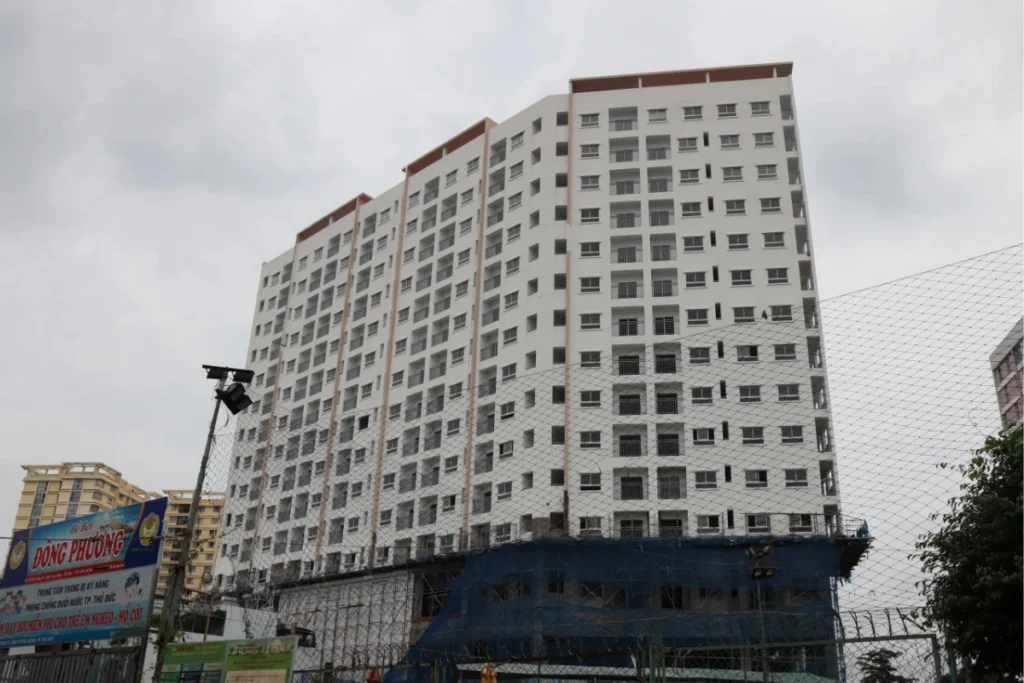 Ảnh chụp cận cảnh từ dưới lên một tòa chung cư cao tầng sơn màu trắng, có thiết kế các ô cửa sổ và ban công nhỏ đều đặn