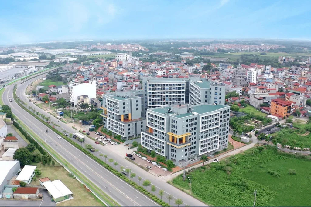 Góc chụp từ trên cao một tổ hợp chung cư nhà ở xã hội hiện đại thấp tầng với mái ngói xanh, nằm đan xen giữa khu dân cư hiện hữu và trục đường lớn