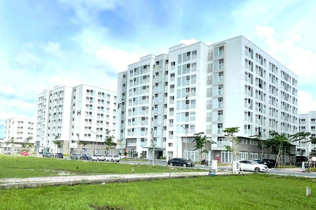 Dãy tòa nhà chung cư nhà ở xã hội màu trắng xám hiện đại xếp cạnh nhau, phía trước là bãi cỏ xanh rộng lớn