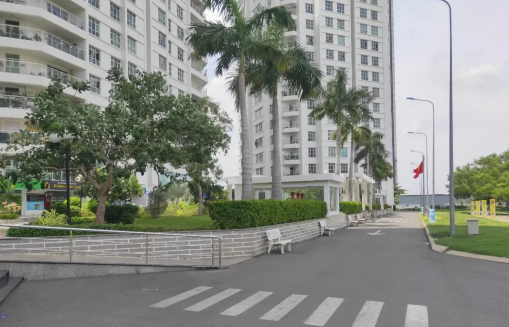Đường nội khu trải nhựa bằng phẳng tại chung cư Hoàng Anh Thanh Bình Quận 7 có vạch kẻ sang đường, hàng cây dừa, ghế đá và bốt bảo vệ an ninh