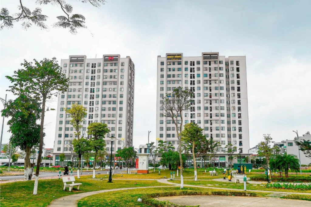 Hai tòa nhà chung cư cao tầng màu trắng xám hiện đại đối diện khuôn viên công viên cây xanh có lối đi bộ, hình ảnh minh họa giải đáp NOXH có bị xuống cấp không