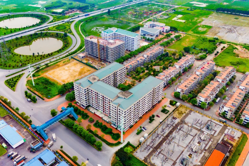 Góc nhìn từ trên cao xuống một khu đô thị hiện đại bao gồm các tòa chung cư, dãy nhà phố liền kề, hệ thống đường giao thông uốn lượn xung quanh các hồ nước và mảng xanh công viên