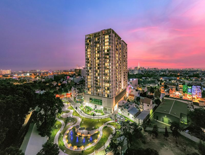 Toàn cảnh block căn hộ Moonlight Residences Thủ Đức lung linh ánh đèn vào buổi tối bên cạnh công viên nội khu rộng lớn có hồ nước và đài phun nước
