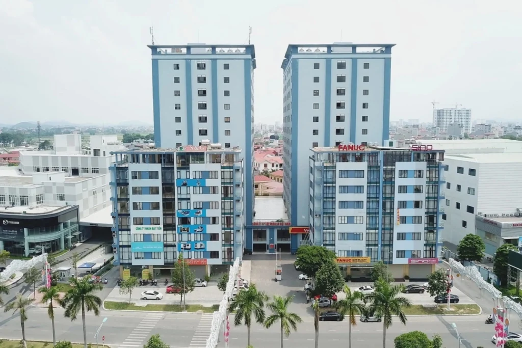 Hai tòa tháp chung cư cao tầng hiện đại sơn màu xanh dương phối trắng đối xứng nhau, phía trước mặt tiền là các khối nhà thấp tầng thương mại