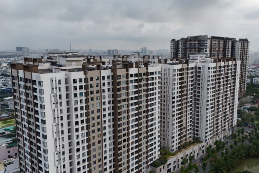 Góc nhìn từ trên cao xuống một cụm các tòa nhà chung cư cao tầng có mật độ xây dựng dày đặc, phía xa là toàn cảnh thành phố dưới bầu trời nhiều mây