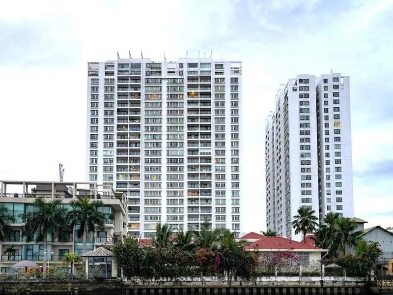 Góc nhìn thực tế từ phía bờ sông hướng về các tòa block chung cư Hoàng Anh Thanh Bình Quận 7, phía trước là dãy nhà thấp tầng mái ngói đỏ và hàng cây xanh dọc bờ kè