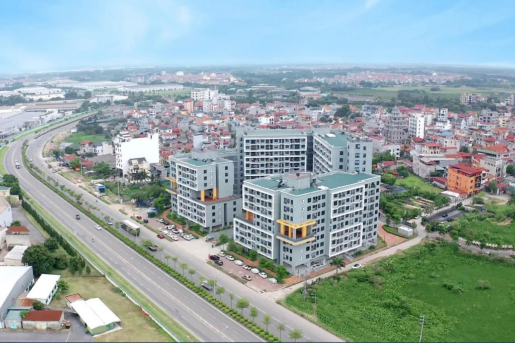 Góc nhìn từ trên cao một tổ hợp chung cư hiện đại với các tòa nhà sơn màu xám và điểm nhấn vàng, nằm dọc theo tuyến đường lớn