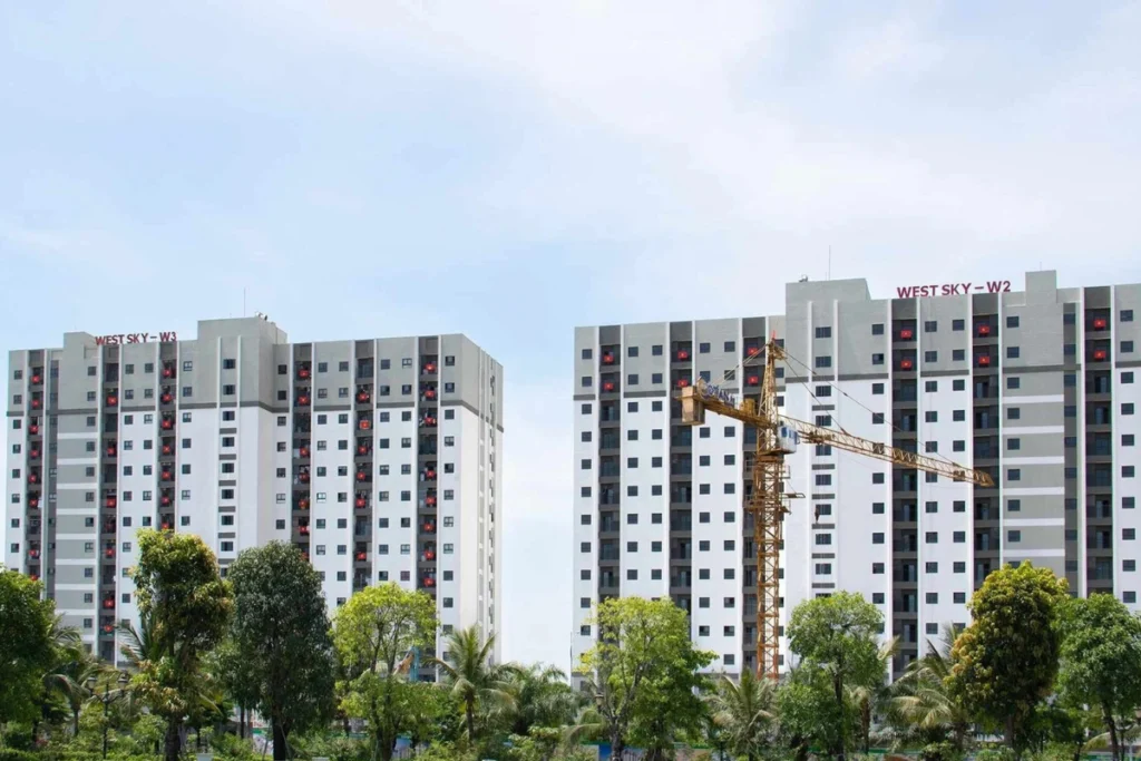 Hai khối tòa nhà chung cư cao tầng West Sky W3 và West Sky W2 sơn màu trắng xám hiện đại, phía trước có một xe cần cẩu công trình màu vàng và hàng cây xanh