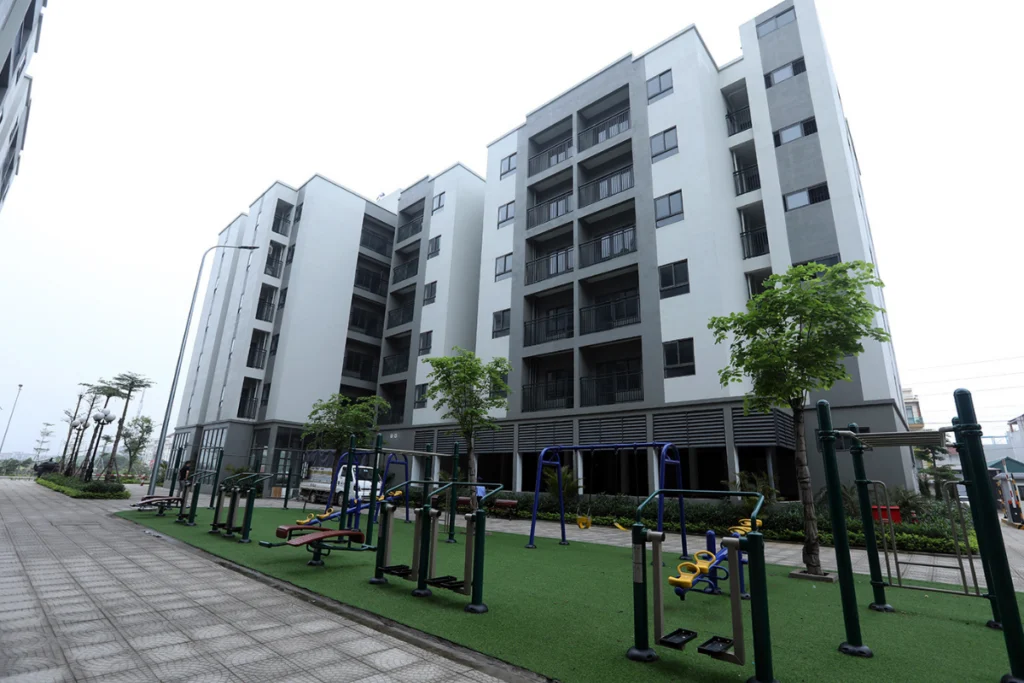 Khoảng sân nội khu của dự án chung cư nhà ở xã hội với lối đi bộ sạch sẽ, hàng cây xanh và khu vực lắp đặt các thiết bị tập thể dục ngoài trời cho cư dân