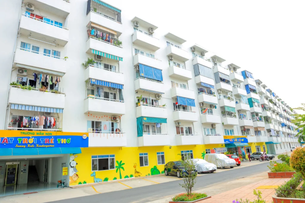 Ảnh chụp cận cảnh mặt trước của một block chung cư Lê Thành An Lạc sơn màu trắng, khối đế tầng trệt sơn màu vàng rực rỡ