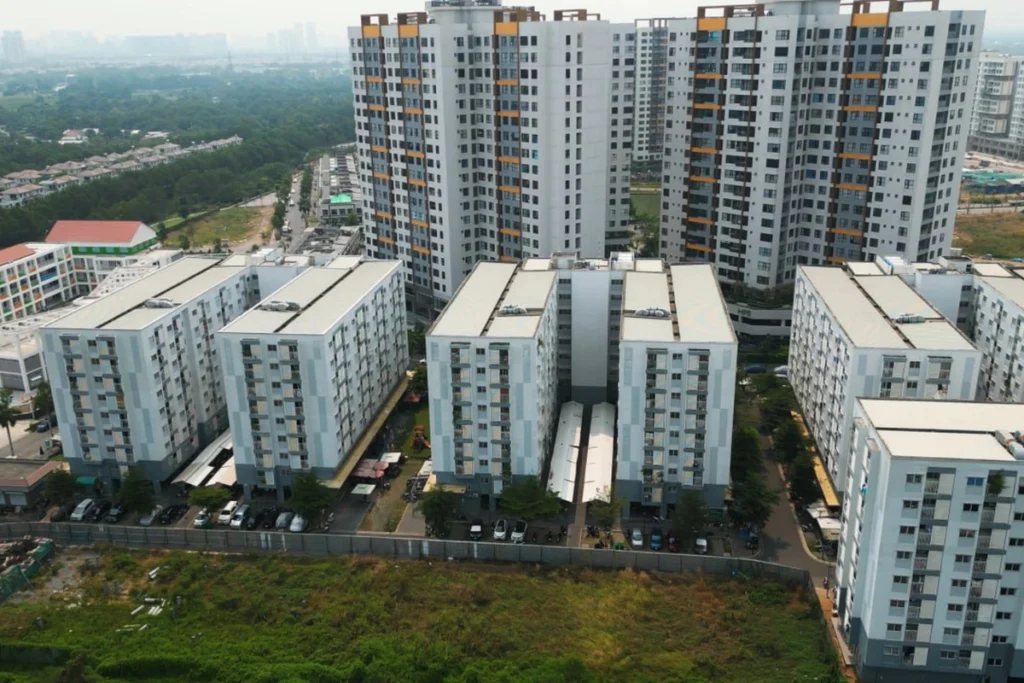 Góc nhìn từ trên cao xuống cụm nhà ở chung cư gồm các block thấp tầng phân bổ song song và hai tòa block cao tầng phía sau, xung quanh có nhiều cây xanh bao phủ mảng lớn
