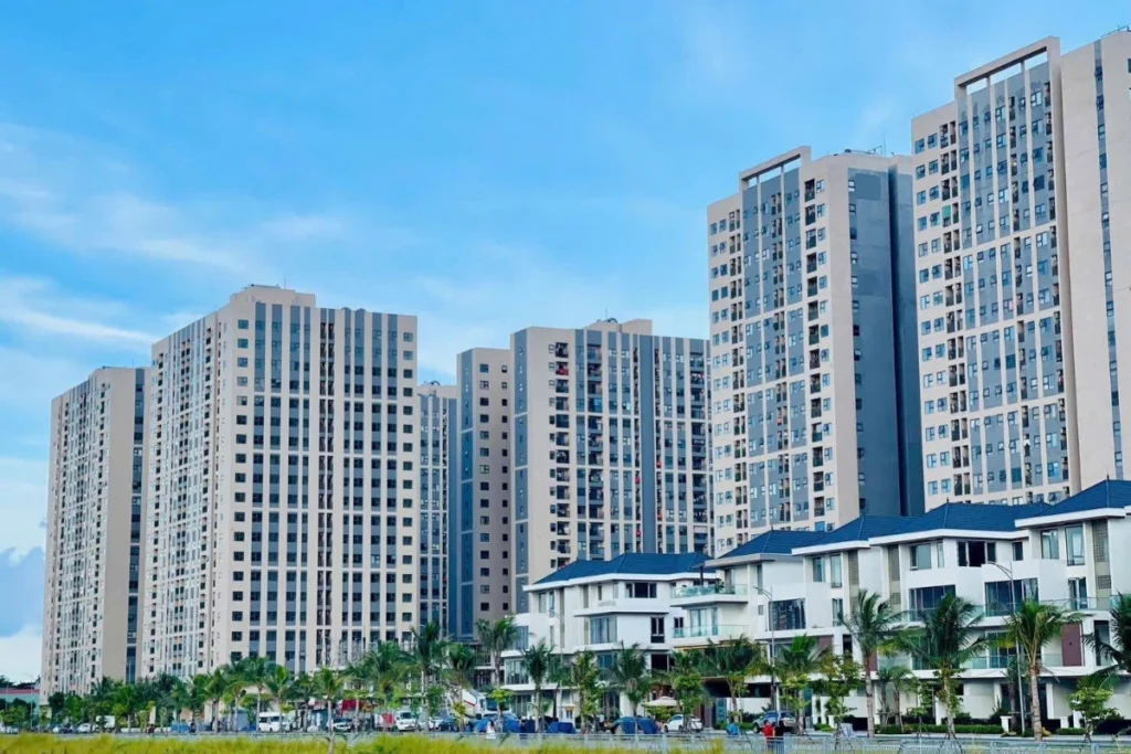 Dãy các block chung cư cao tầng có thiết kế đồng bộ hiện đại sơn màu xám trắng, phía trước có hàng biệt thự thấp tầng lợp mái ngói xanh và cây cảnh