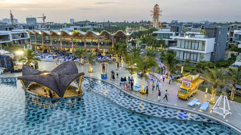 Hình ảnh thực tế sự kiện ngoài trời sầm uất bên cạnh hồ bơi vô cực lớn tại dự án The Maris Vũng Tàu, phía sau là nhà hàng kiến trúc lượn sóng và mô hình cối xay gió biểu tượng.