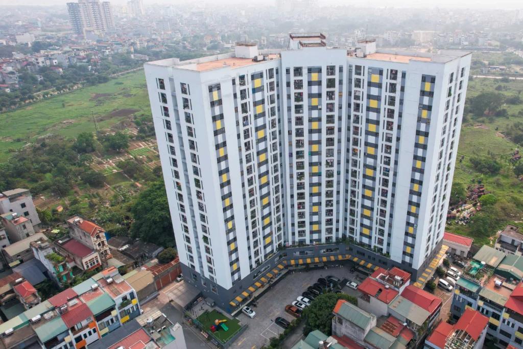 Ảnh chụp thực tế từ trên cao một khối tòa nhà chung cư nhà ở xã hội có quy mô lớn, kiến trúc uốn lượn hình chữ V, tường sơn trắng kết hợp các ô vuông màu vàng và xám xen kẽ