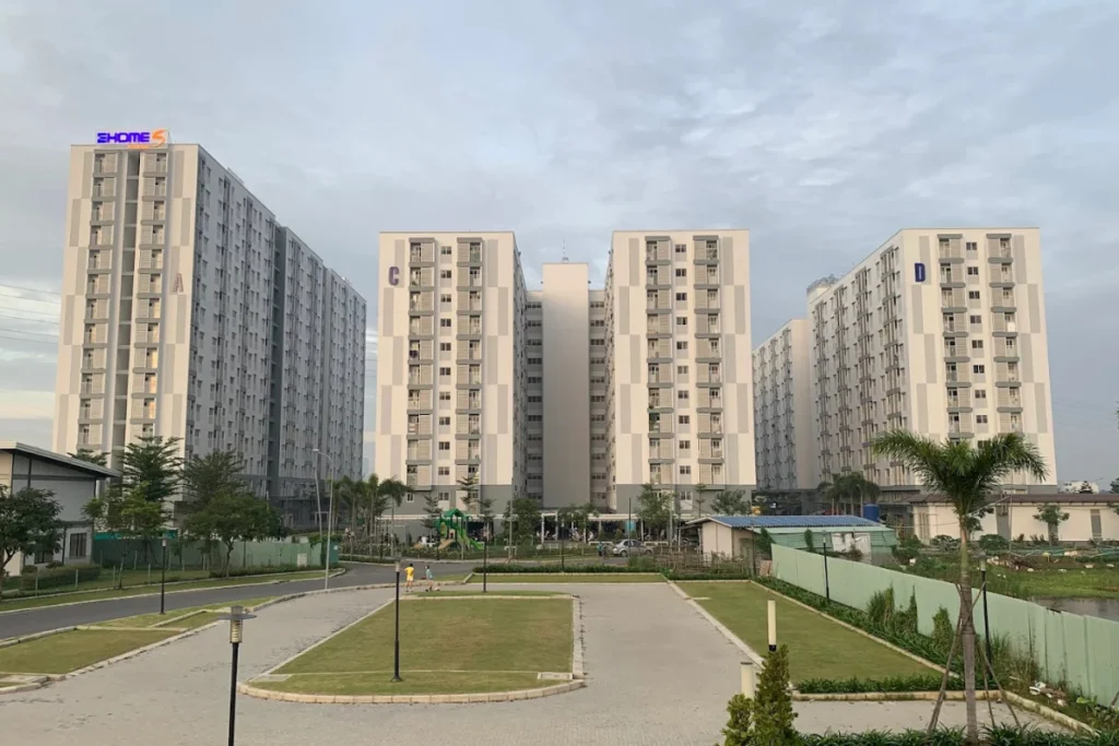 Góc nhìn chính diện từ khu sân nội khu rộng rãi lên ba block chung cư cao tầng kiên cố mang tông màu trắng chủ đạo phối các mảng xám kẻ caro hiện đại