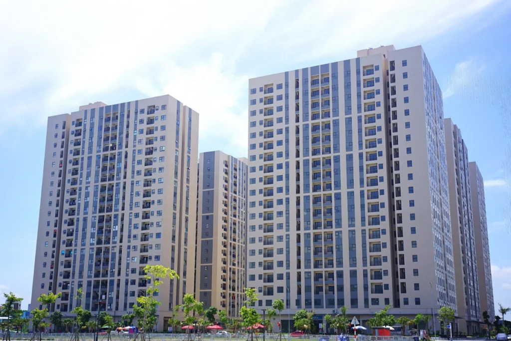 Tổ hợp nhiều tòa nhà chung cư nhà ở xã hội cao tầng kiên cố mang thiết kế đồng bộ hiện đại, phía trước là quảng trường rộng rãi có trồng một số cây xanh nhỏ