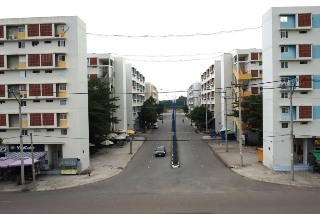 Góc nhìn từ ngã ba đường nội khu hướng vào các block nhà ở xã hội Becamex 5 tầng đối xứng hai bên, có dải phân cách giữa đường với hàng cây xanh nhỏ