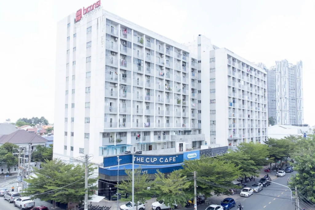 Hình ảnh chụp thực tế tháp chung cư nhà ở xã hội Phú Hòa Lợi Biconsi tại Thủ Dầu Một với các cửa hàng tiện ích đang hoạt động, minh họa cho câu hỏi có nên mua NOXH Phú Hòa Lợi
