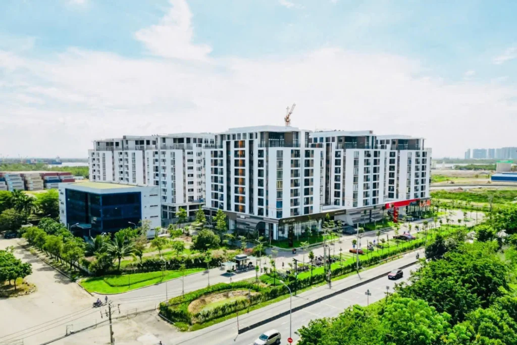Ảnh chụp từ trên cao một khu chung cư cao tầng hiện đại sơn màu trắng xám, khối đế có các cửa hàng kinh doanh thương mại và sảnh kính lớn
