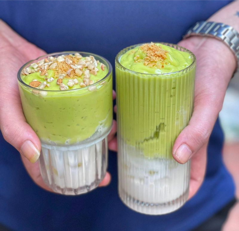 Người cầm hai ly bơ già dừa non màu xanh lá tươi phủ dừa khô rang giòn hấp dẫn