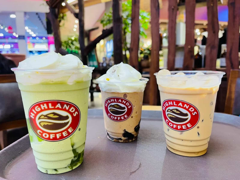 Ba ly nước uống Highlands Coffee gồm freeze trà xanh, freeze cà phê có thạch và phin sữa đá đặt trên khay nhựa màu nâu